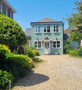 a green house with a white door and a gravel driveway at The Coach House- Stunning Detached Coastal home, with parking, by Historic Deal Castle in Deal