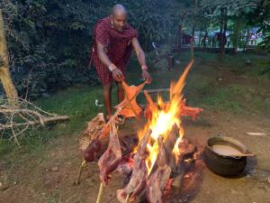 Un uomo sta cucinando carne su un falò di Hillstone Safari Lodge a Kimana