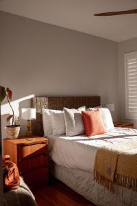 a bedroom with a bed with white sheets and orange pillows at Driftwood Rest Binalong Bay Sleeps 4 in Binalong Bay