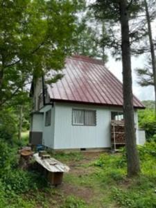 een wit huis met een rood dak in het bos bij 大自然の一軒家。便利社会からの逃避、究極のセルフ山小屋ライフ in Madarao Kogen