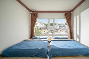 two beds in a room with a large window at Raon Dalat - STAY 24H in Da Lat
