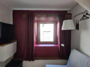 a bedroom with a window with red curtains and a television at Casa di Volce - 1801 Stone House in Tolmin