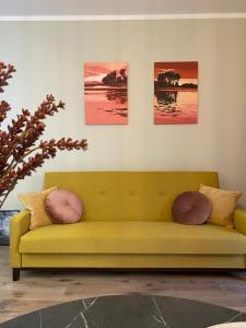 a yellow couch in a room with three pictures on the wall at Apartament Olecko Nad Jeziorem in Olecko