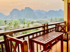 a wooden bench on a balcony with a view of mountains at Hana Riverside Hotel in Vang Vieng