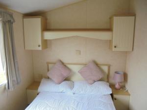 a bedroom with a bed with white sheets and pink pillows at Coral Beach : The Richmond:- 6 Berth, Blow heated in Ingoldmells