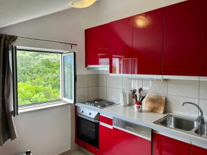 コルチュラにあるApartmani Lukaのキッチン(赤いキャビネット、シンク、窓付)