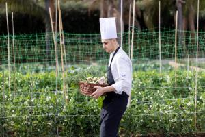 a man wearing a chef hat holding a basket of vegetables at Donna Carmela Resort & Lodges in Riposto