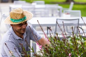 a man wearing a straw hat looking at flowers at Donna Carmela Resort & Lodges in Riposto
