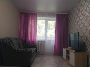 sala de estar con cortinas rosas, sofá y TV en Подобово квартира в центрі міста, en Konotop