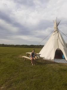 a woman sitting on a picnic table next to a teepee at Hawk's View Tipi at Higher Hawksland Farm in Saint Issey