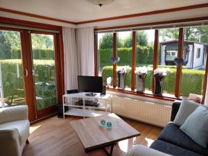 een woonkamer met een bank, een tv en ramen bij Chalet in Drenthe te huur aan de rand van het bos Drents Friese Wold, veel PRIVACY en RUST in Hoogersmilde