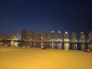 een skyline van de stad 's nachts met een strand en gebouwen bij Luxury Sea View Apartment with Amazing Amenities at Pearl Qatar in Doha