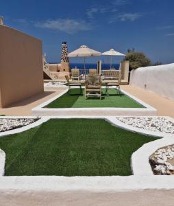 a patio with chairs and green grass and umbrellas at Thetis Cave Houses in Oia