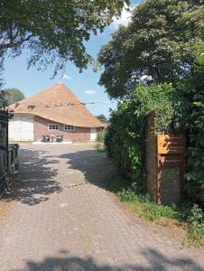 a brick driveway leading to a building with a thatched roof at Tiny House Aqualinde in Breda