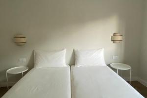 duas camas com lençóis brancos num quarto com dois bancos em Casa com jardim perto da praia em Sesimbra