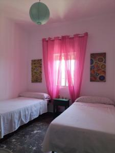 a room with two beds and a window with pink curtains at Villa Antonia in Chipiona