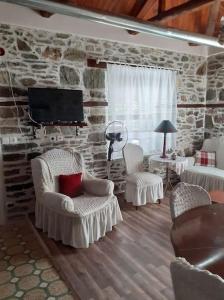 a living room with white chairs and a stone wall at Ξυλοπετρα / Wood & stone house in Tsagarada