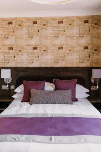 een groot bed met paarse en witte kussens erop bij The Bull Hotel in Stony Stratford