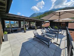 szereg krzeseł i parasol na patio w obiekcie Ferienwohnungen Karlingerhof am See w mieście Achenkirch