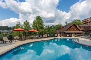 a pool with chairs and umbrellas in front of a house at 2 Miles from Dollywood Family Resort with Seasonal Outdoor Swimming Pool, Year around Heated Indoor Swimming Pool, Townhome Style Cabin, Private Hot Tub, Arcade, TV, Wifi, Kitchen with Refrigerator, Washer and Dryer in Pigeon Forge