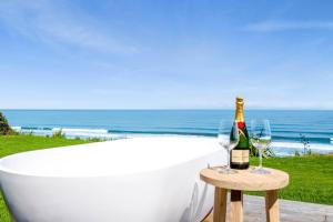 MOKAU BEACH HOUSE في Mokau: حوض استحمام مع زجاجة من الشمبانيا وكأسين