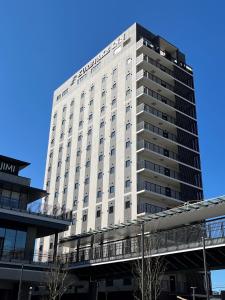 a tall white building with a bridge in front of it at Kuretake Inn Premium Tajimi Ekimae in Tajimi