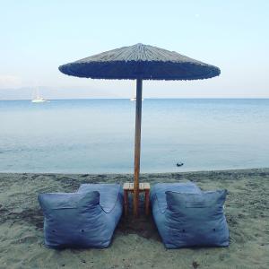 マラトカンボスにあるNereides Seaside Apartmentsのビーチのパラソルの下に青い椅子2脚