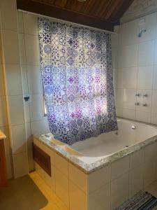 a bathroom with a bath tub with a shower curtain at Chalé na Av. Principal de Monte Verde com Lareira e Banheira in Camanducaia