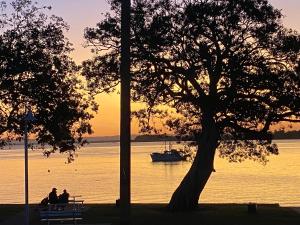 deux personnes assises sur un banc en regardant un bateau dans l'eau dans l'établissement Sylvan Seas, à Bellara