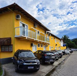 una fila de autos estacionados al lado de un edificio amarillo en Pousada Rafimar, en Ilhabela