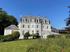 une grande maison blanche sur une colline avec un parasol dans l'établissement Hôtel Château Cléry, à Hesdin-lʼAbbé