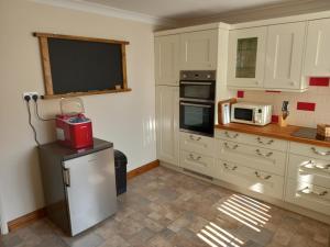 a kitchen with white cabinets and a tv on the wall at Pet Friendly Beautiful Detached Cottage close to Spurn Point, Easington and Withersea in Hull +17 photos