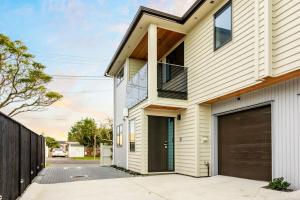 une maison blanche avec un garage marron dans l'établissement Pristine Modern Central Home - Netflix - Heatpump, à Auckland