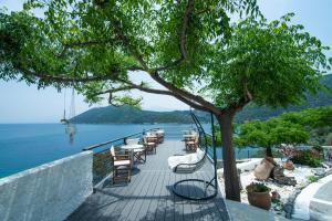 eine Terrasse mit Stühlen und ein Baum neben dem Wasser in der Unterkunft Nafsika Villas in Kerveli