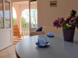 a table with two cups and a vase with flowers at Apartment Rose in Krk