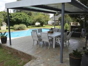 un patio con mesa, sillas y piscina en Rudys Guesthouse en Meyerton