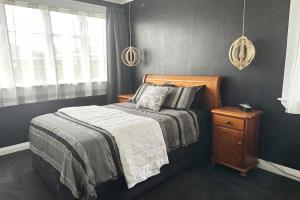 a bedroom with a bed and a night stand and windows at The Tirau Cottage - Waikato in Tirau