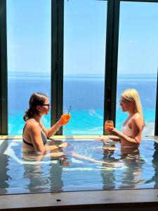 two women sitting in a swimming pool with drinks at Rigas Boutique Hotel & Spa in Afitos