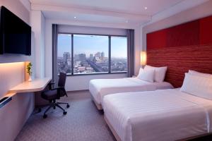 a hotel room with two beds and a desk and a window at Grand Mercure Jakarta Harmoni in Jakarta