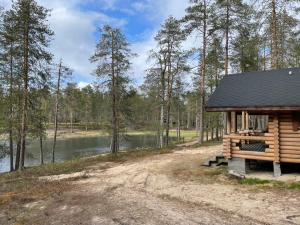 una cabaña de madera con un lago al fondo en Kolmiloukon leirintäalue en Taivalkoski
