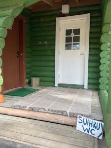 a white door on a green house with a sign in front at Kolmiloukon leirintäalue in Taivalkoski