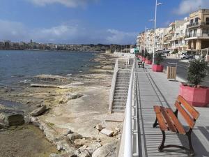 a wooden bench sitting on a sidewalk next to the water at Caris Gem in Birżebbuġa +2 photos