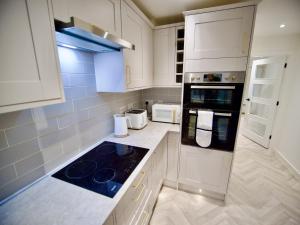 La cuisine est équipée de placards blancs et d'un four avec plaques de cuisson. dans l'établissement Ideal Lodgings in Radcliffe, à Radcliffe