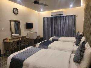 Habitación de hotel con 3 camas, escritorio y espejo. en Hotel Akbar International, en Rawalpindi