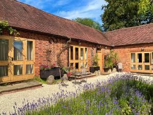 a brick house with a garden and purple flowers at The Clock Tower & The Dairy - Two x 2 Bed Barns with Indoor Pool in Checkendon