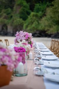 Cape Panwa Hotel Phuket في شاطئ بنوا: طاولة طويلة عليها زهور أرجوانية وبيضاء