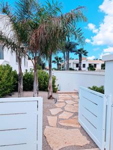 una pasarela de piedra con una puerta blanca y palmeras en Pescoluse Apartments en Marina di Pescoluse