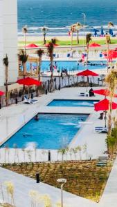 Porto Said Resort Rentals في بورسعيد: مجموعة من المسابح مع المظلات الحمراء والمحيط