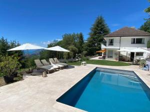 Stunning Villa overlooking lake في Le Châtelard-Montreux: مسبح بكراسي ومظلات بجانب بيت