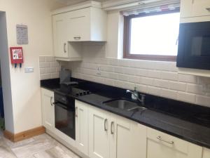 uma cozinha com armários brancos, um lavatório e uma janela em Old Bakery Roundstoneselfcatering em Roundstone